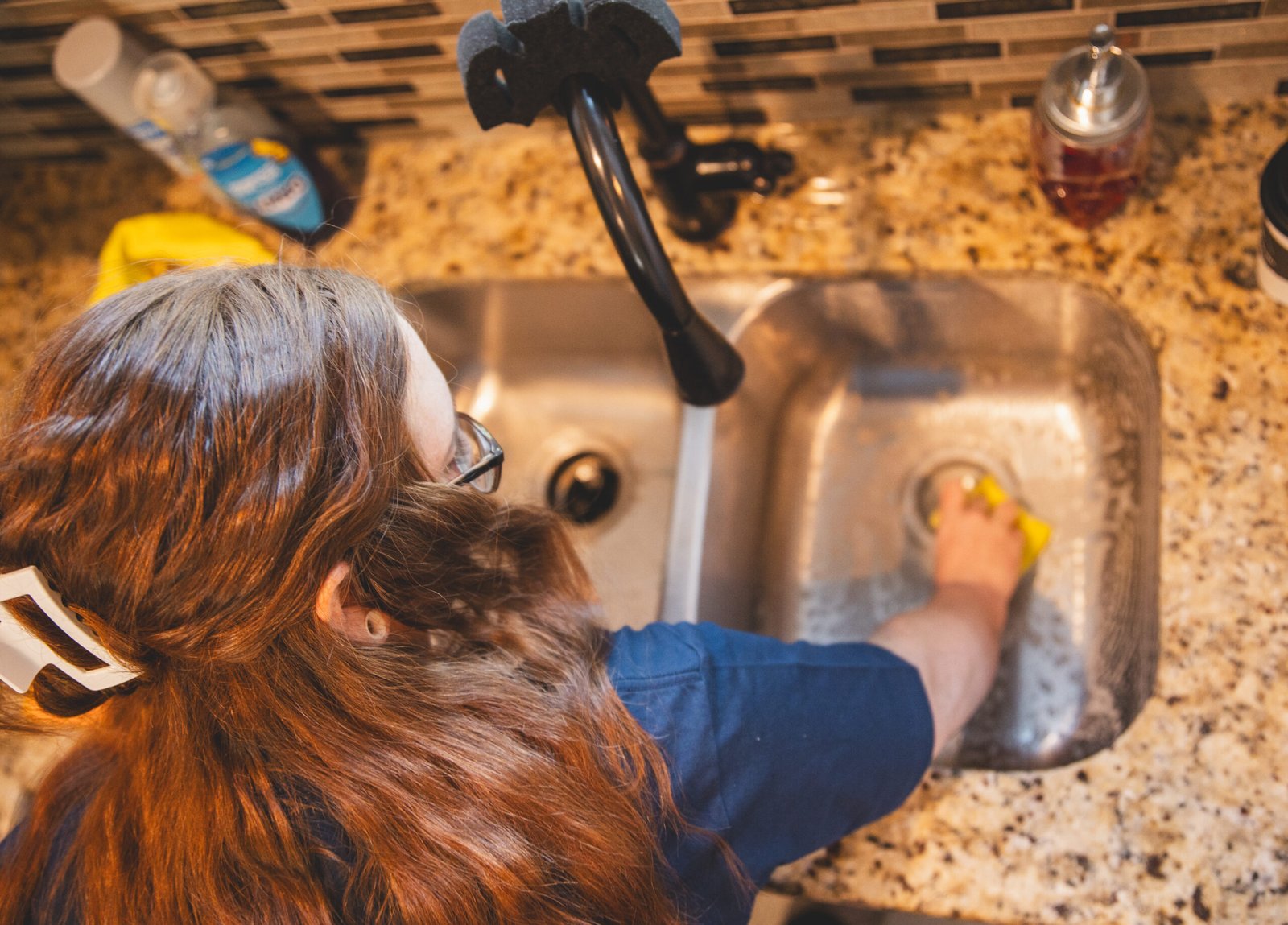 A worker from The Mop & Broom cleans a kitchen sink in Burleson, showcasing their professional cleaning services.